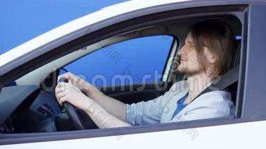 年轻的长发男子驾驶着带蓝色钥匙的白色汽车。 他穿着蓝色T恤和条纹夹克。 Brunette男子